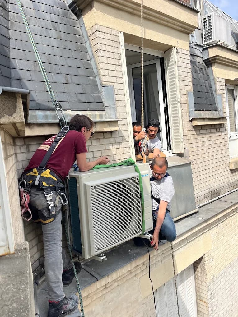 Techniciens installant un groupe extérieur de climatisation en hauteur sur une façade d'immeuble