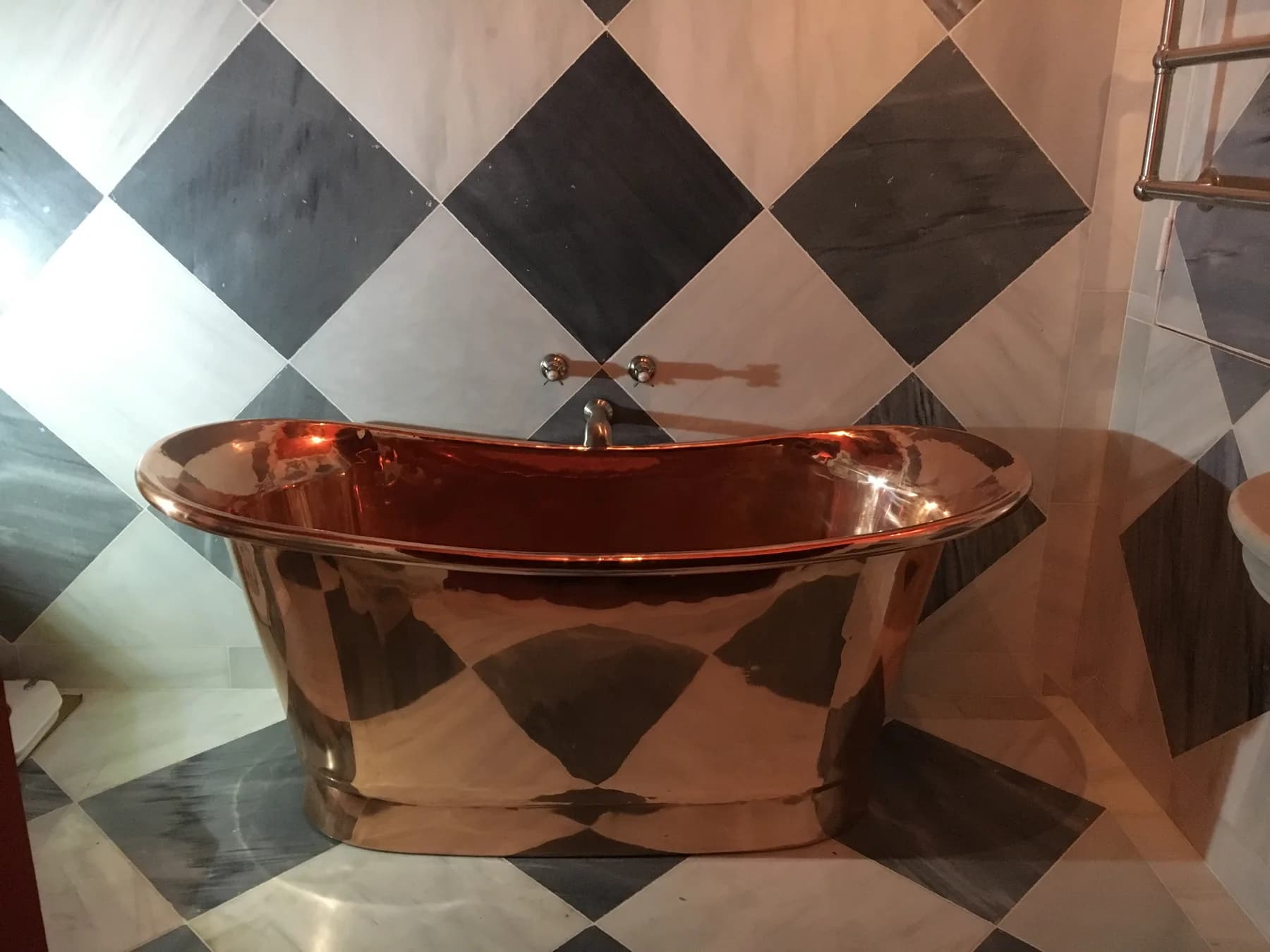 Baignoire îlot en cuivre poli dans une salle de bain au carrelage damier